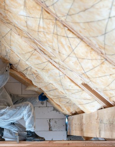 Side view of one worker man in overalls working with rockwool insulation material, standing inside new house under construction fasten warmth layer on ceiling and wall